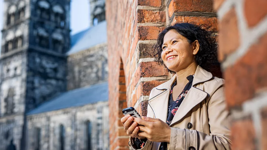 Kvinna står lutad mot en mur med telefon i handen