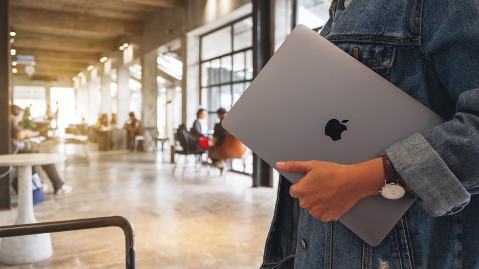 En person håller i en macbook i kontorslandskap