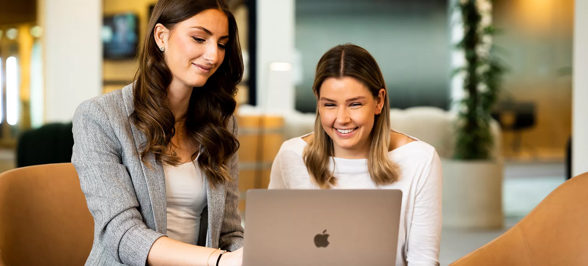 Två leende kvinnor framför en Macbook