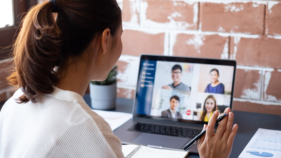 En kvinna sitter vid sin dator och vinkar till sina kollegor över video