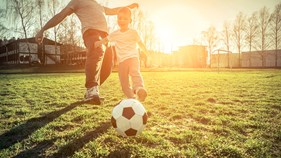 Pojke och man spelar fotboll i solsken